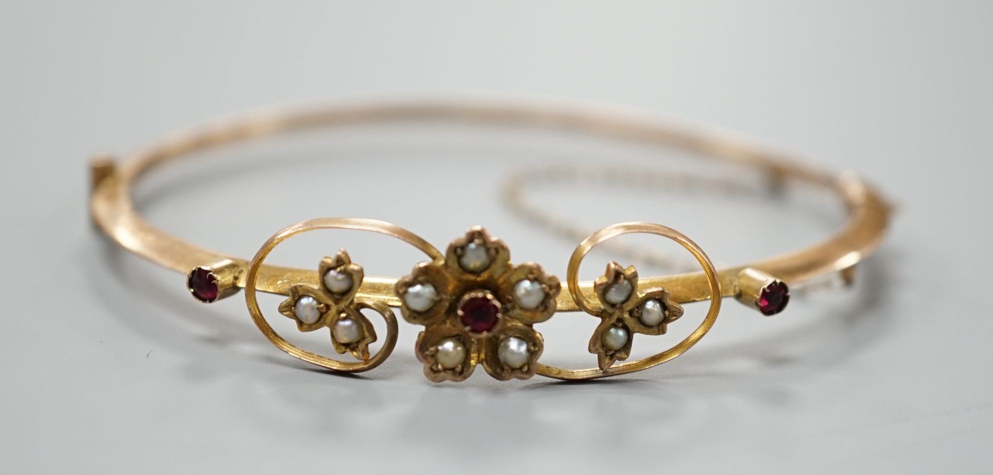 An Edwardian 9ct, red stone and seed pearl set hinged bangle, interior diameter 55mm, gross weight 4.4 grams.